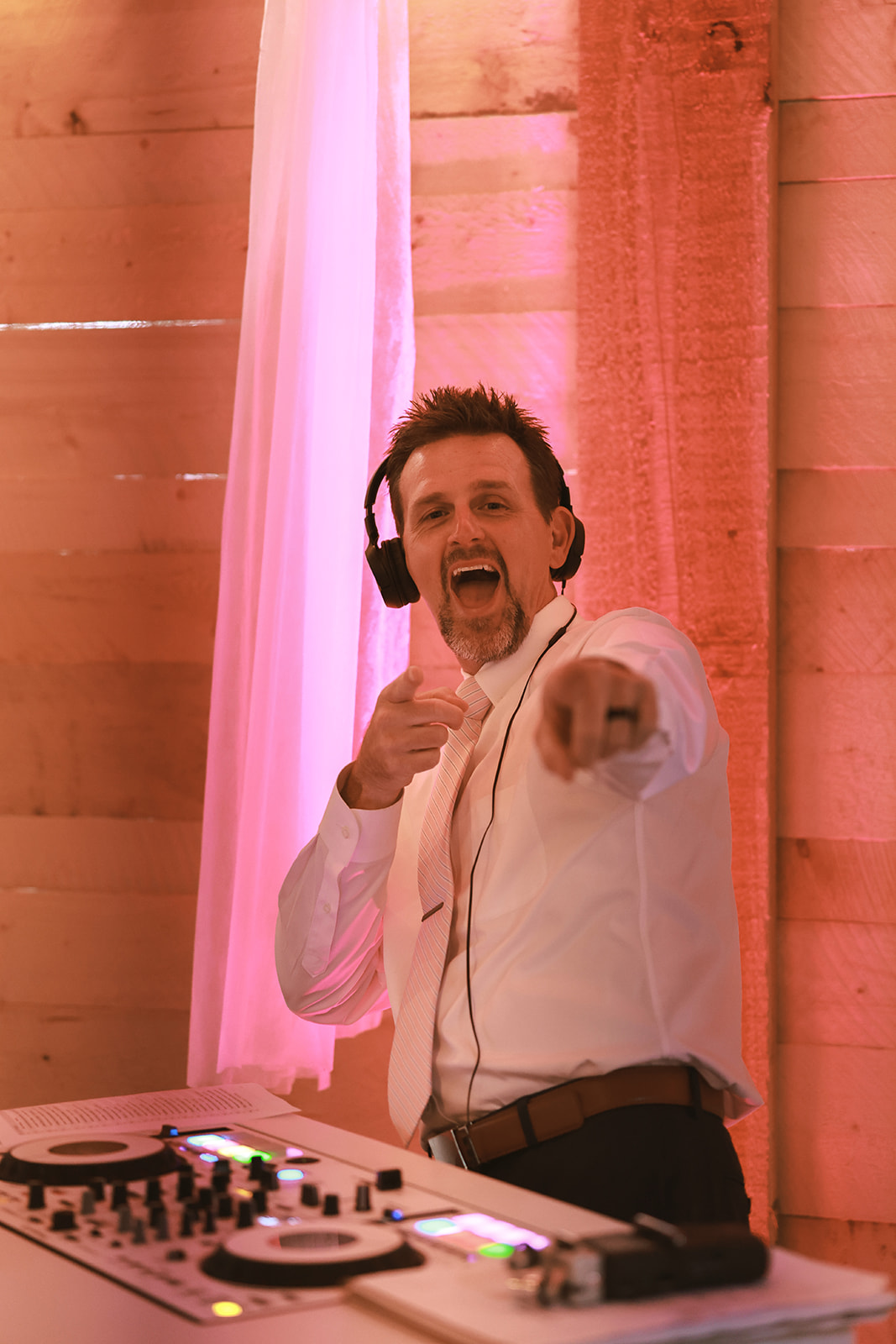 Noyes + McCullar Wedding Wedding DJ in headphones cueing the next track under pink uplighting at an Alaska wedding reception