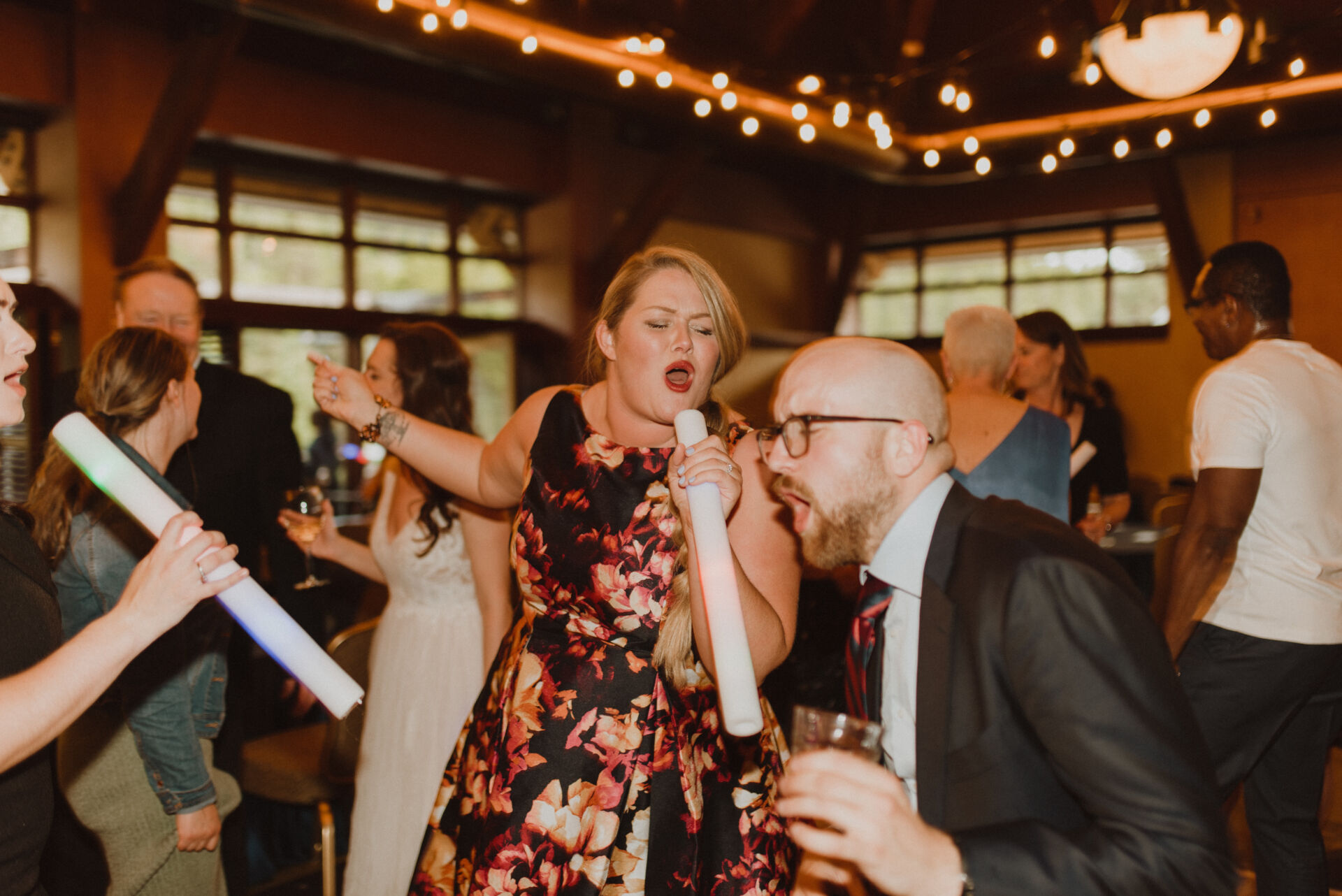 Peter & Victoria Caltagirone Wedding guest singing along under string lights at an Alaska wedding reception